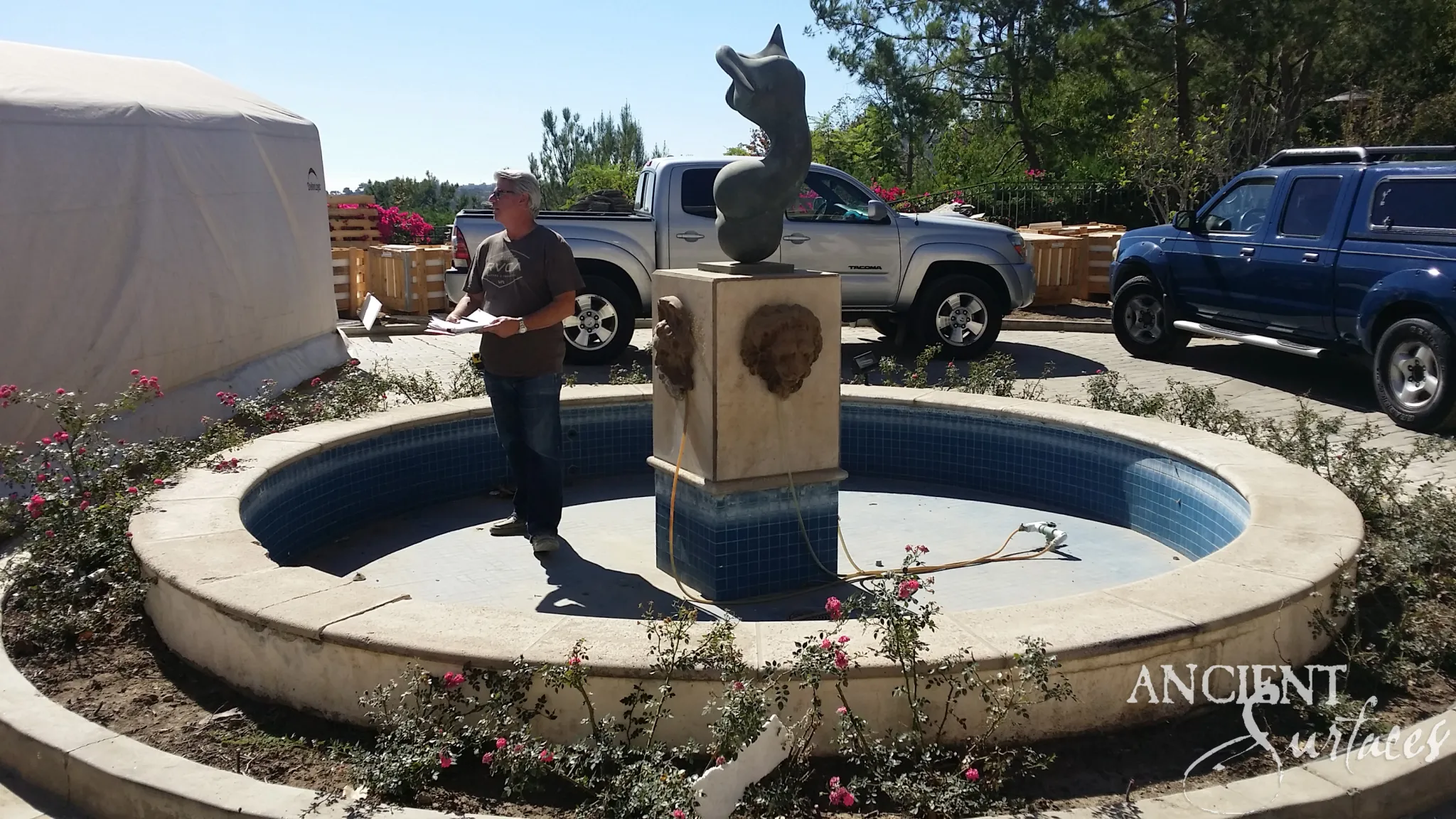 Reclaimed limestone pool fountain with a lion-mask pedestal and leaping-fish sculpture in a rose-ringed round pool