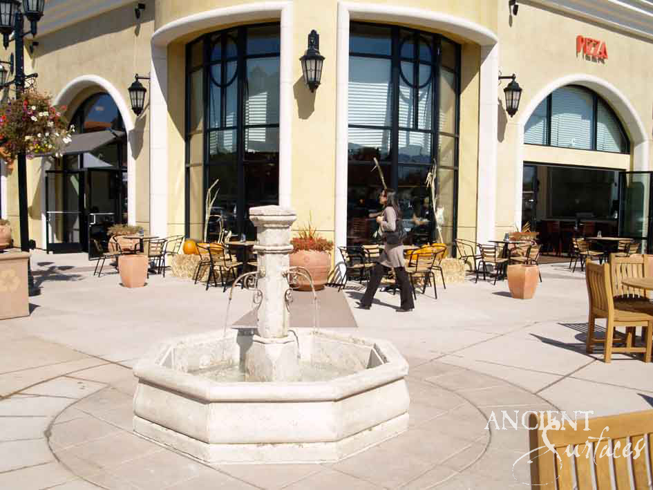 Reclaimed limestone pool fountain with paired spouts running on a sunlit paved piazza